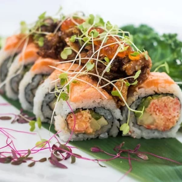 Lemongrass Asian Bistro sushi roll topped with salmon, crispy fried pieces, orange roe, and microgreens.