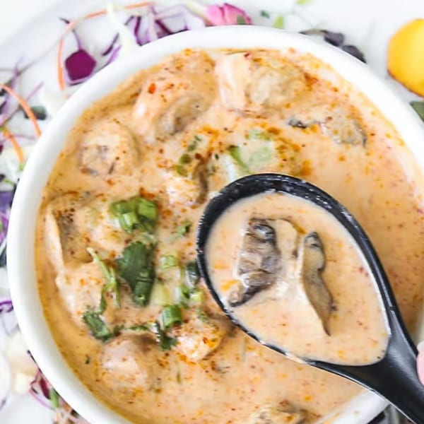 Creamy Lemongrass Asian Bistro soup with mushrooms and green onions, served with a black spoon.
