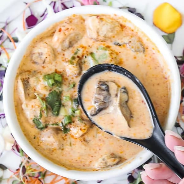 Creamy Lemongrass Asian Bistro soup with mushrooms and herbs, served in a white bowl with a black spoon.