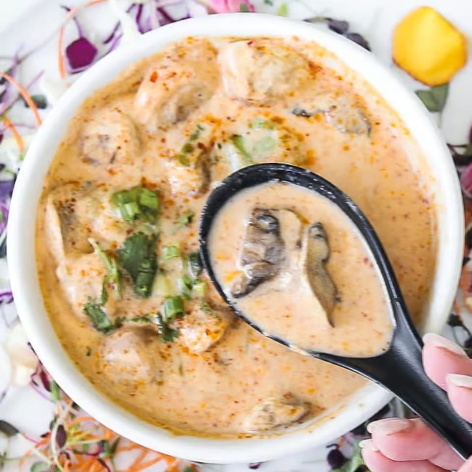 Creamy Lemongrass Asian Bistro soup with mushrooms and herbs, served in a white bowl with a black spoon.