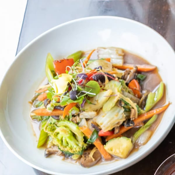 A white bowl filled with colorful stir-fried vegetables, including broccoli, carrots, and mushrooms.