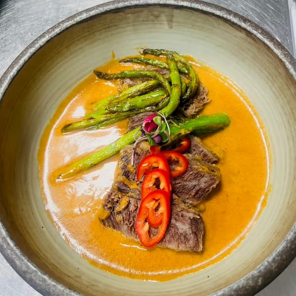 Lemongrass Asian Bistro's beef dish with asparagus, red peppers, and a rich orange sauce in a bowl.