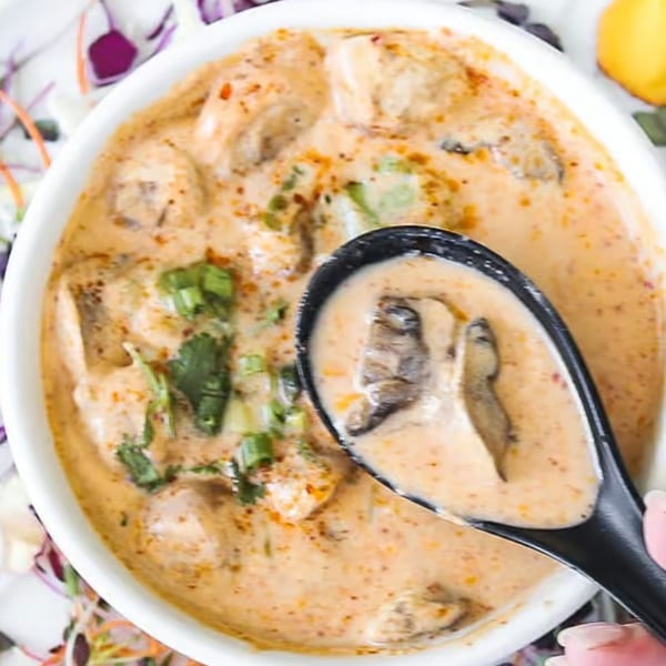 Creamy mushroom soup with green onions and cilantro in a white bowl, with a spoon lifting some soup.