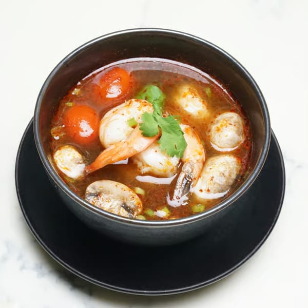 Lemongrass Asian Bistro's Tom Yum soup with shrimp, mushrooms, and tomatoes in a black bowl.