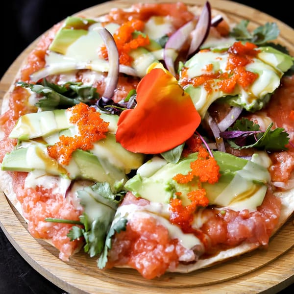 Lemongrass Asian Bistro sushi pizza with salmon, avocado, roe, and red onion on a wooden board.