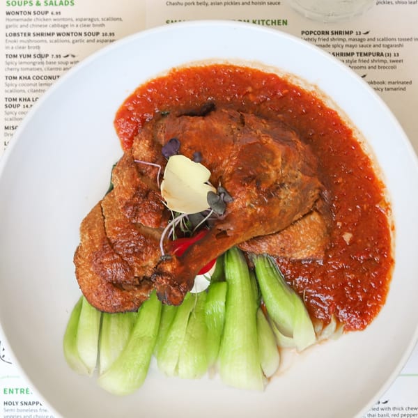Crispy duck leg with red sauce and green bok choy on a white plate at Lemongrass Asian Bistro.
