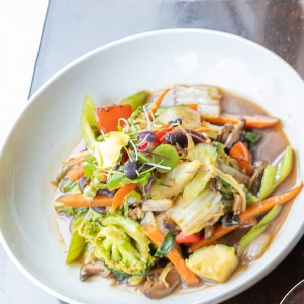 A white bowl filled with colorful stir-fried vegetables, including broccoli, carrots, and mushrooms.
