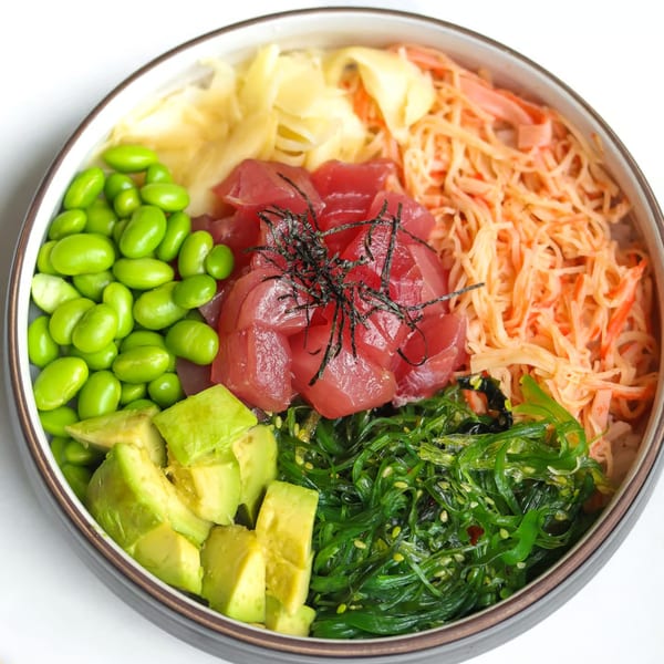 A colorful poke bowl with tuna, edamame, avocado, seaweed salad, and pickled ginger.