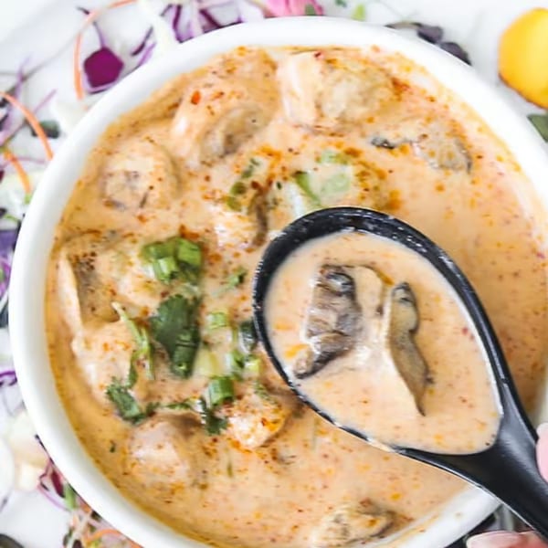 Creamy mushroom soup with green herbs in a white bowl, with a black spoon scooping some.