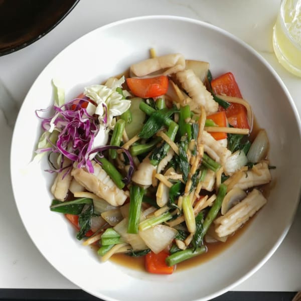 A white bowl filled with stir-fried squid, mixed vegetables, and a side of red and green cabbage.