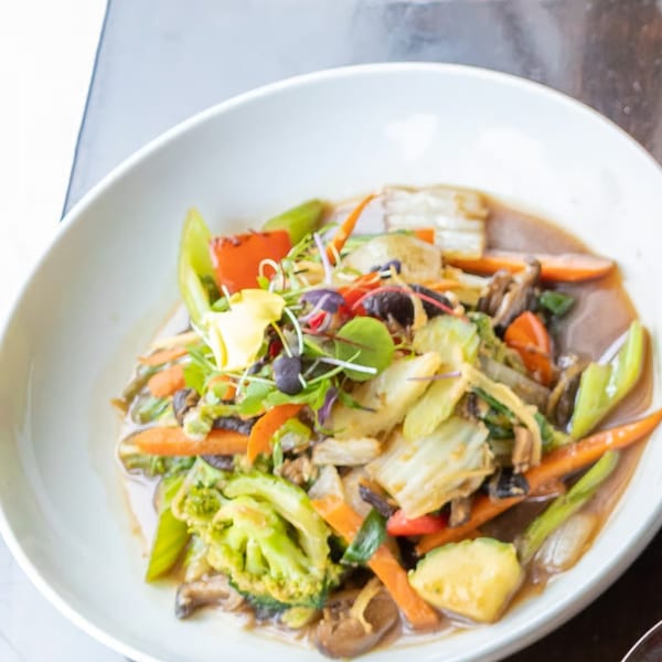 A white bowl of colorful stir-fried vegetables with a savory sauce, garnished with microgreens.